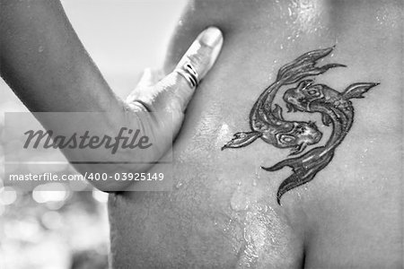 Close up of nude wet Caucasian mid adult womans tattoo of koi fish on lower back.