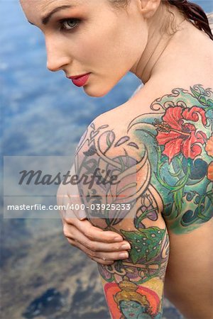 Back view of sexy nude tattooed Caucasian woman by tidal pool in Maui, Hawaii, USA.