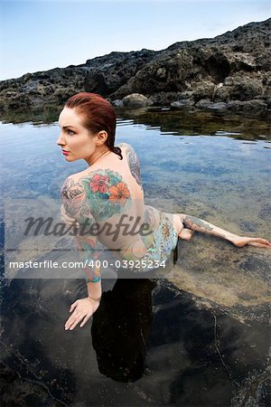 Back view of nude sexy Caucasian tattooed woman in bikini lying in tidal pool in Maui, Hawaii, USA.