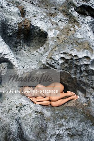 Young Asian nude woman sleeping in a crevice in a rock.