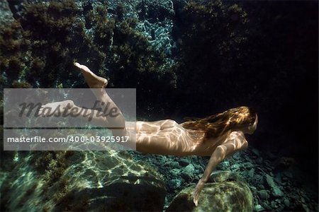 Underwater view of young Asian nude woman swimming away.