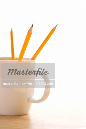 Three pencils in a coffee cup with pointed ends up.