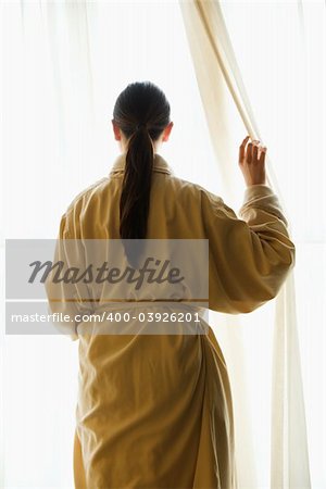 Taiwanese mid adult woman in bathrobe  looking out window.