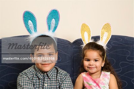 Hispanic brother and sister wearing bunny ears smiling and looking at viewer.