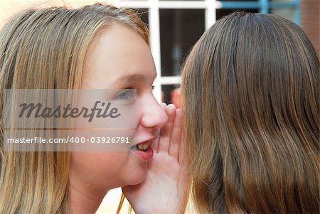 Two young teenage girls gossiping in school yard