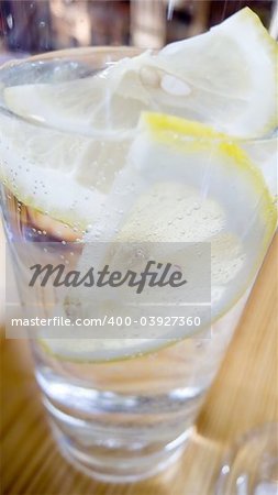 A close up vertical panoramic shot of a cool glass of sparkling mineral water with ice and lemon