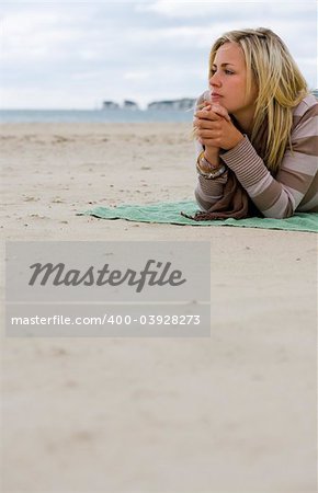 A beautiful blond haired blue eyed young woman laying alone on a beach deep in thought