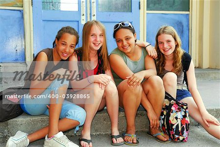 Portrait of a group of young smiling school girls sitting on steps near school building