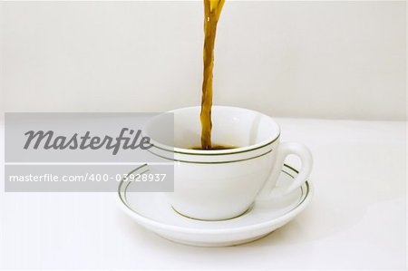 Black coffee being poured on a white cup over white background