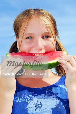 Young girl biting into a slice of watermelon on blue sky background