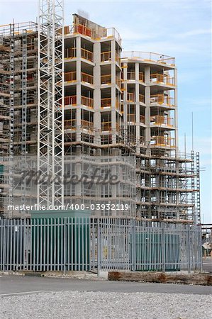 New tall building under construction with scaffolding, against a pale blue sky.