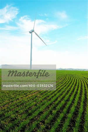 Wind turbine standing against a blue skywith some clouds in a green grass field