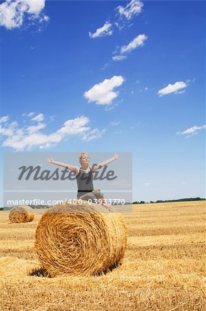 Woman enjoying the summer sun sitting on a hay bale under a bright blue sky