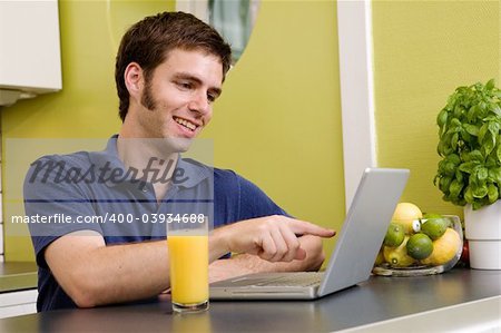 A young male using a laptop computer in the kicthen, smiling and laughing at what he sees