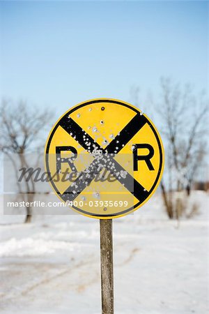 Railroad crossing sign in snow covered rural landscape.