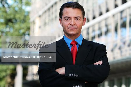 Good looking caucasian / white business man standing with arms folded against an office building.