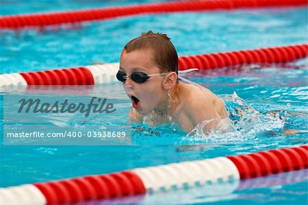 Action photo of a young boy wearing goggles swimming in a pool.