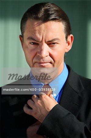 Good looking caucasian / white business man standing against an office background adjusting his tie.