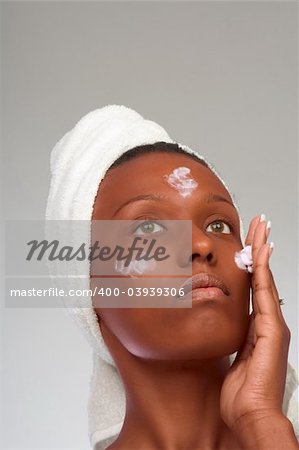 African-American girl applying facial skincare product (gray background)