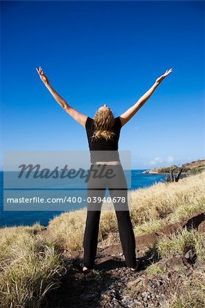 Back view of Caucasian mid-adult woman standing on Maui, Hawaii coast with arms outstretched and head thrown back.