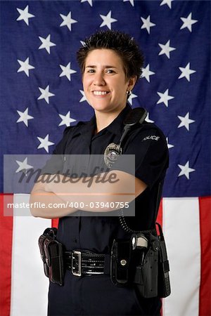 Portrait of mid adult Caucasian policewoman standing with arms crossed with American flag as backdrop smiling at viewer.