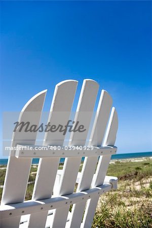 Empty white adirondack chair facing beach.