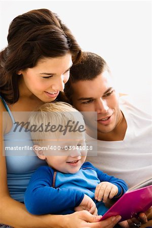 Caucasian parents and toddler son reading book together.