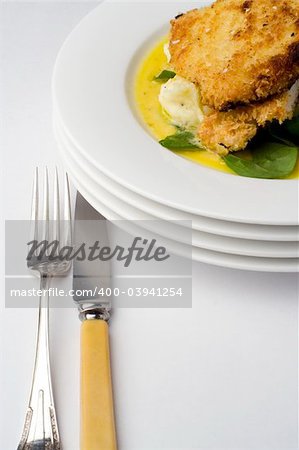 Chicken schnitzel, baked with potato mash, baby spinach and beure blanc sauce. Portrait view with antique knife and fork.