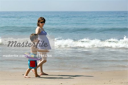 Pregnant mother and her son walking on the beach