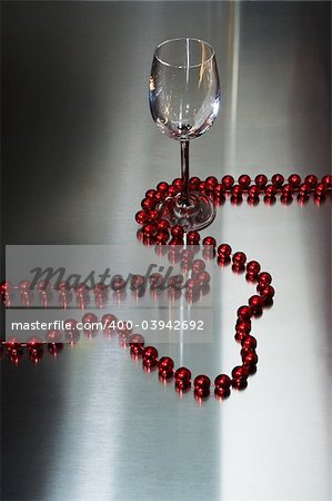 Wine-glass and red beads on a metal background