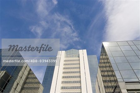 Glass fronted skyscrapers reach up into a bright blue sky with a few whispy clouds