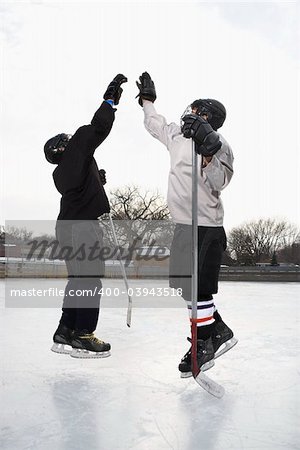 Two boys in ice hockey uniforms giving eachother high five on ice rink.
