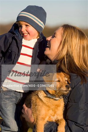 A mother her young son and the family dog together laughing on a park bench.