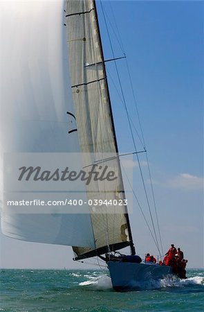 A fully crewed racing yacht with a white spinnaker catching the wind