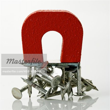Red magnet holding metal nails on white background.