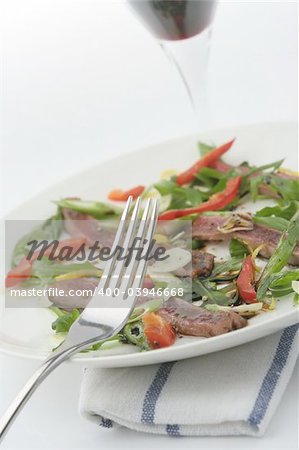 Finely sliced raw bleu beef with rocket and baby capsicum. Baby red capsicum or pepper. Angled view with red wine in glass into out-of-focus white washout.