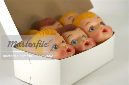 A close up of plastic doll faces in a box ready for assembly