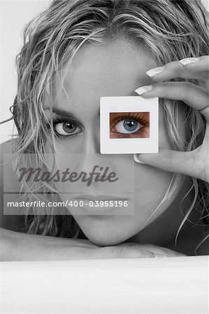 Black and white studio shot of a  stunningly beautiful young blond woman with her bright blue eye looking through a transparency frame