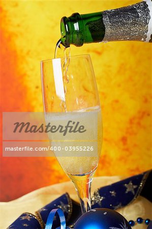 Pouring champagne on glass, over colour background. Shallow DOF