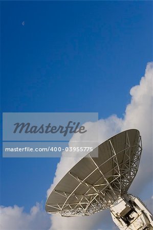 A radio telescope points into an early morning sky where the moon is still present