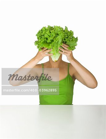 Woman in green holding a lettuce in front of the face