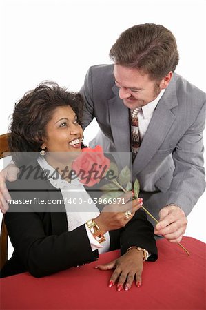 An attractive interracial couple on a date.  He surprises her with a red rose.
