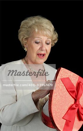 A beautiful senior woman choosing a chocolate from a box of Valentines candy.  Black background