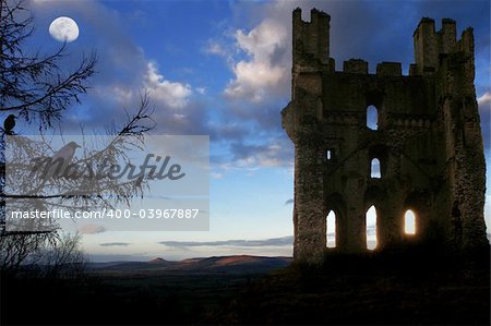 Scottish  Tower ruins said to be haunted at Dusk with rolling Hills in background, glowing shafts of light from Moon through lower windows and Crows nesting in turret and in Fir Tree in forground