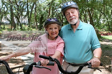 An attractive senior couple bicycling together wearing helmets.