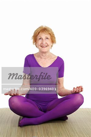 A fit seventy year old woman in a modified lotus pose smiling in contentment.  White background.