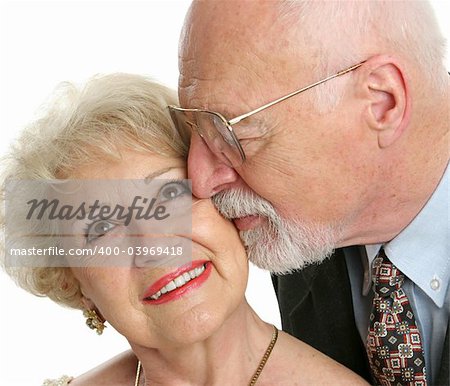 Closeup of a loving senior man gives his beautiful wife a kiss on the cheek.