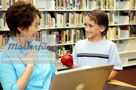 A school boy surprising his teacher with an apple.