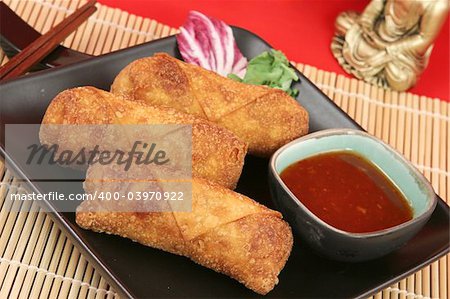 A plate of crispy fried egg rolls with spicy sweet chili sauce for dipping.