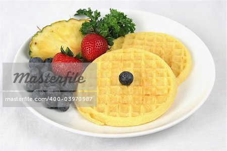 A plate of golden waffles served with blueberries, strawberries and pineapple garnish.